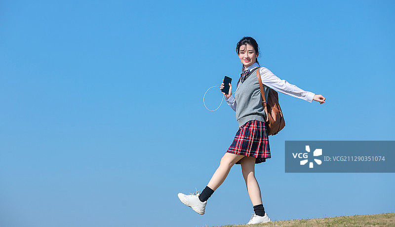 蓝色天空背景下，正在慢跑的亚洲女学生图片素材