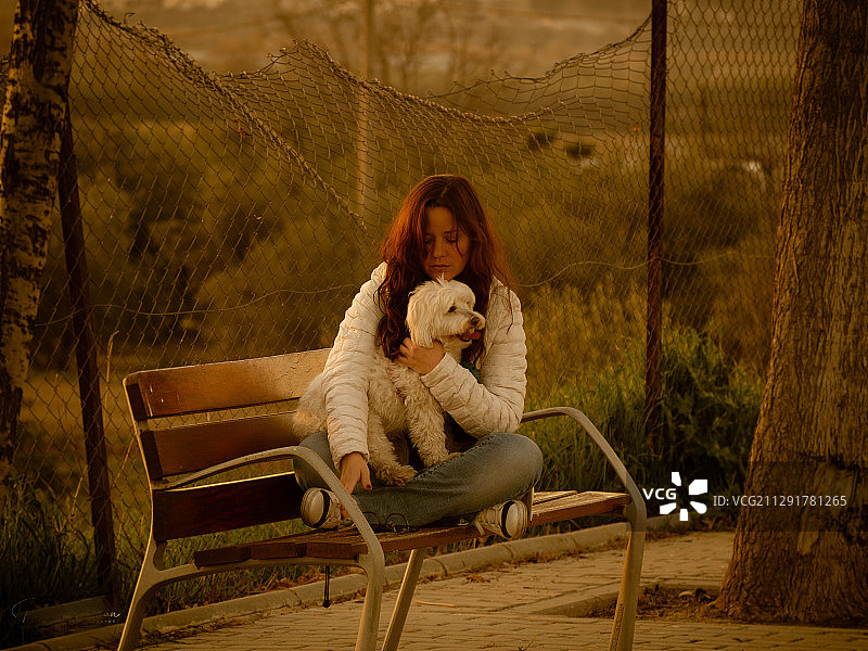 一个年轻的女人和一只白色的狗坐在长凳上图片素材