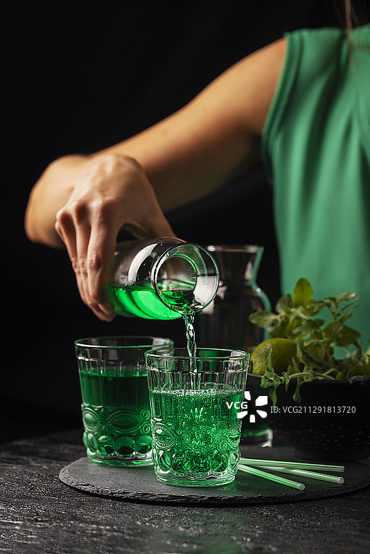 将绿色鸡尾酒倒入玻璃杯的女人的手图片素材