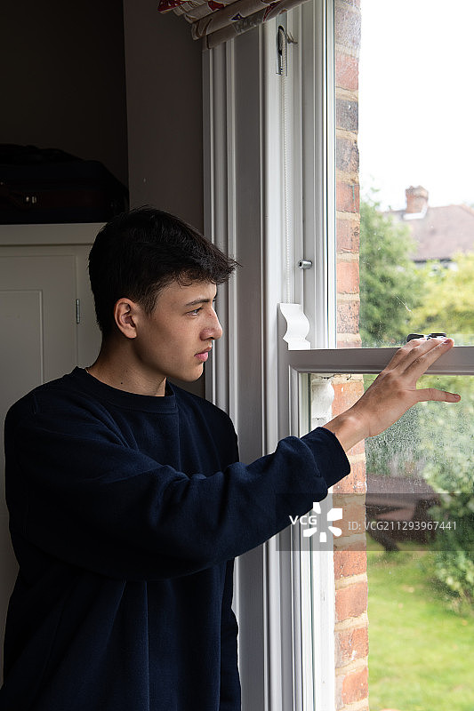 一个被隔离的年轻人从卧室的窗户往外看图片素材