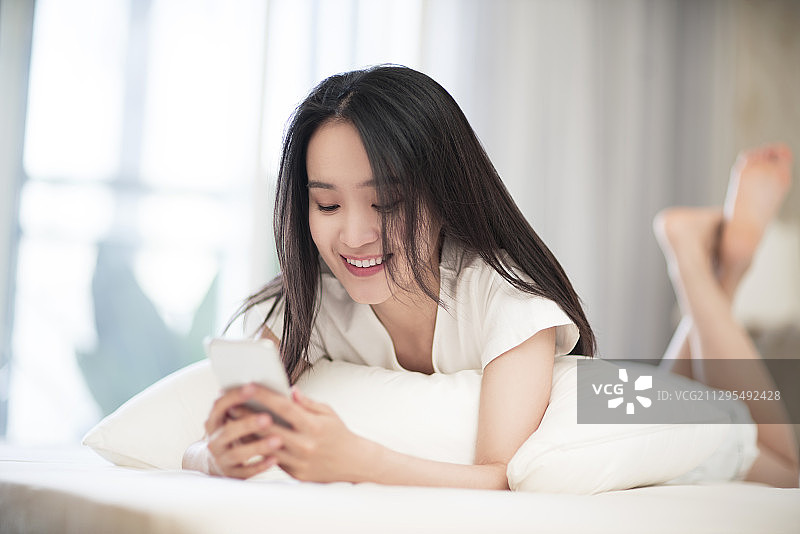 年轻女子躺在床上使用智能手机图片素材