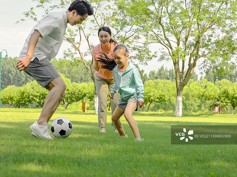 快乐的三口之家在公园踢足球图片素材
