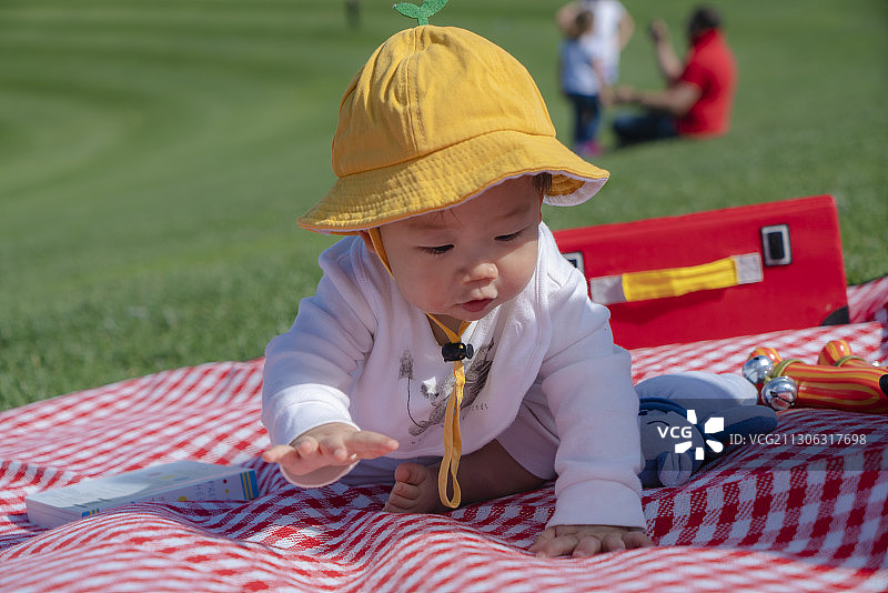 戴黄帽的婴儿在草坪野餐垫爬行图片素材
