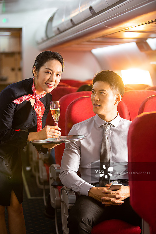 空姐给男商务乘客鸡尾酒在飞机机舱图片素材