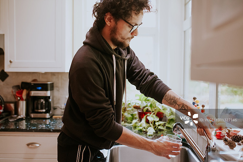 在加拿大不列颠哥伦比亚省维多利亚的家庭厨房里，一名男子正在往杯子里倒水喝图片素材