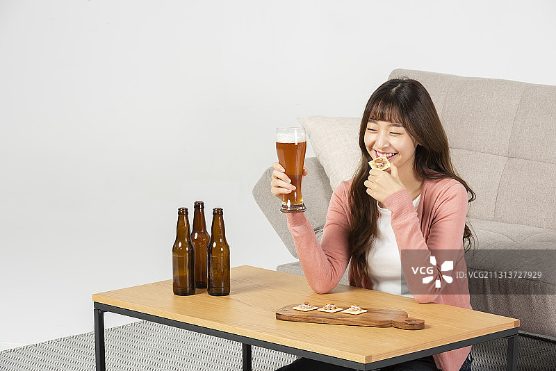 女人坐在桌边微笑着喝啤酒和零食在沙发前图片素材