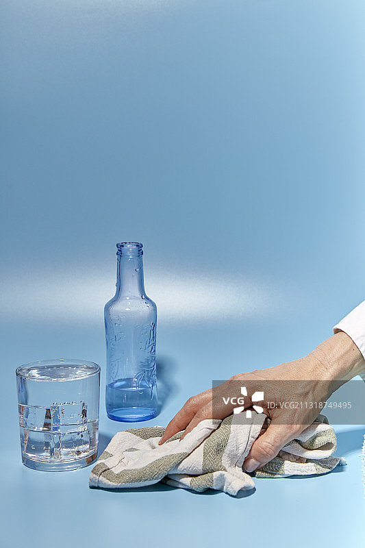 裁剪的女人的手在蓝色背景上擦拭泼出来的水，西班牙图片素材