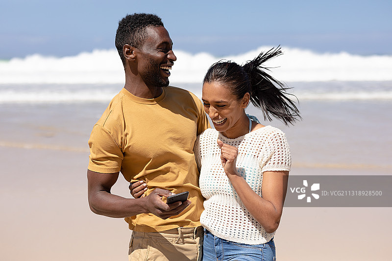 一对非裔美国夫妇在海边的沙滩上玩智能手机图片素材