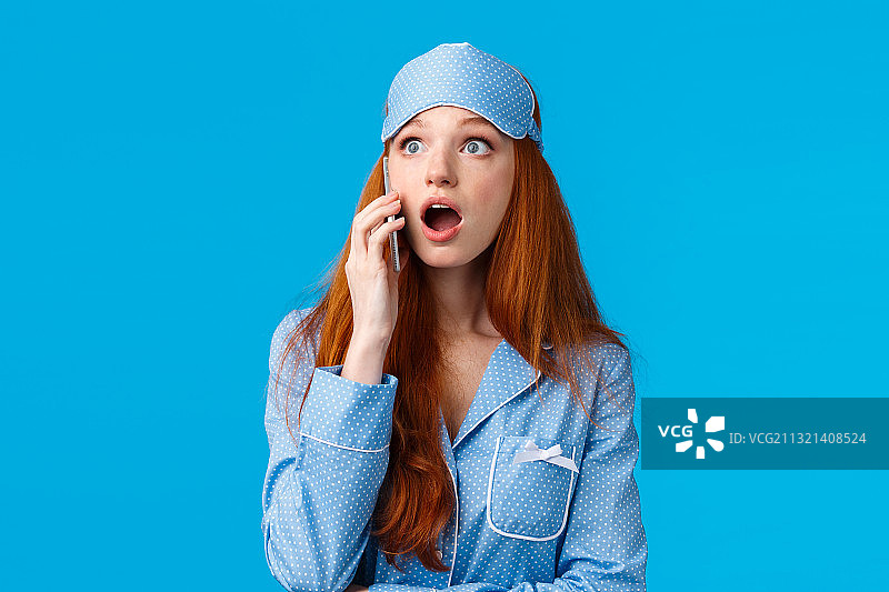 一个震惊的年轻女子在蓝色背景下打电话的肖像图片素材