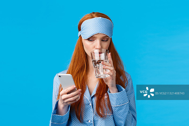 一个年轻女子在蓝色背景下喝着玻璃杯里的水图片素材