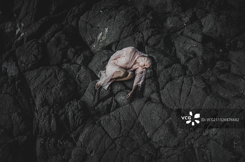 乌克兰，一名身穿粉色雨衣的男子躺在黑色岩石上图片素材