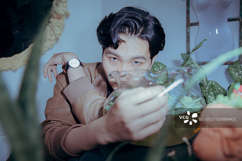 年轻的亚洲人坐在室内植物旁边抽烟图片素材