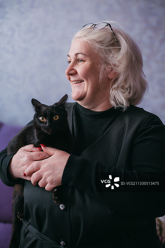 微笑成熟的女人与猫坐在沙发上，哈萨克斯坦图片素材
