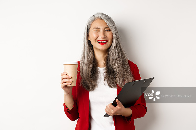 微笑的女商人拿着咖啡杯的肖像，而站在白色的背景图片素材