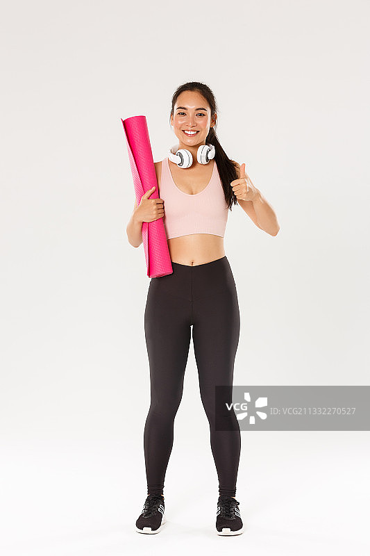微笑的女人拿着运动垫的肖像，而站在白色的背景图片素材