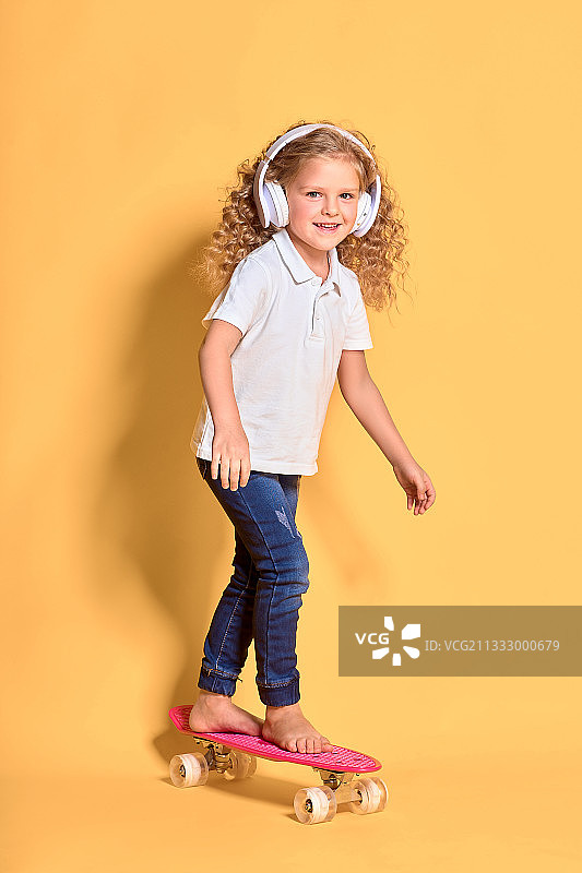 一个有趣的年轻女孩的肖像与滑板的黄色背景图片素材