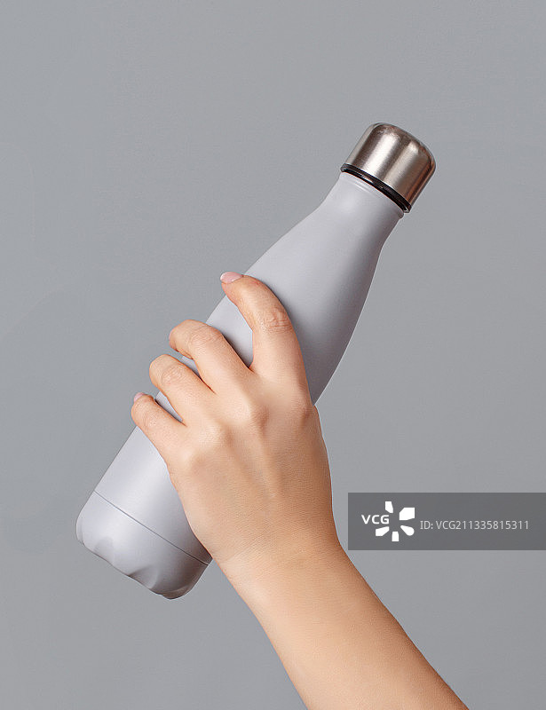 手与灰色可重复使用的绝缘瓶在灰色背景图片素材