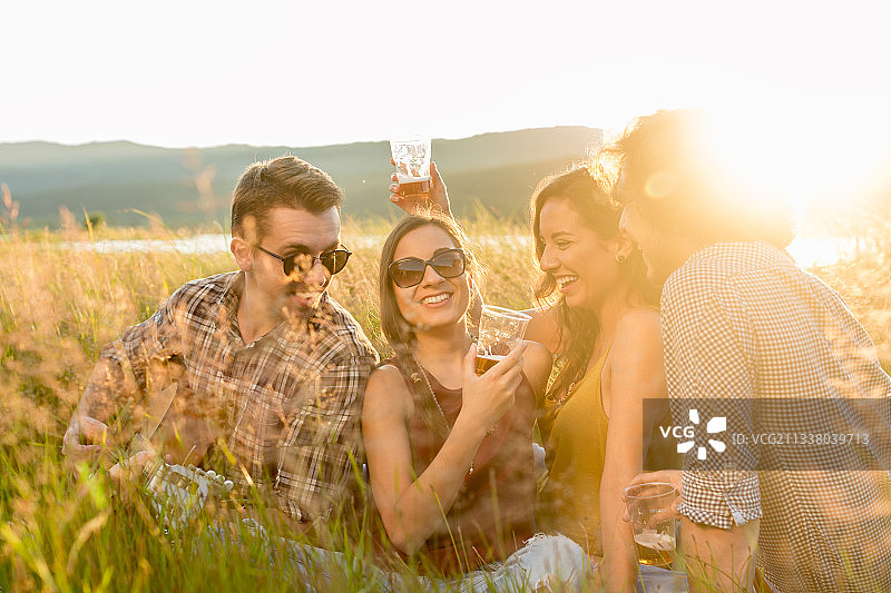 朋友们坐在高高的草地上，喝着饮料，听着吉他音乐，享受着夏日傍晚的心情图片素材