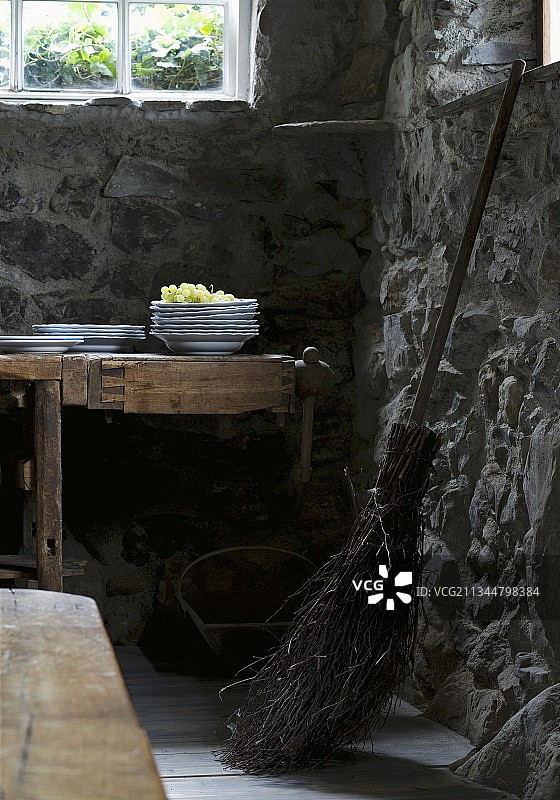 在有石墙的酒窖里，旧扫帚旁边的桌子上堆放着盘子和葡萄图片素材