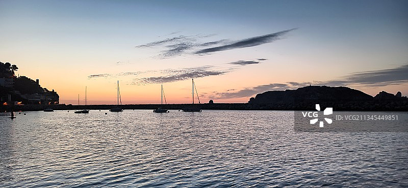 日落时，天空映衬下海上帆船的剪影图片素材