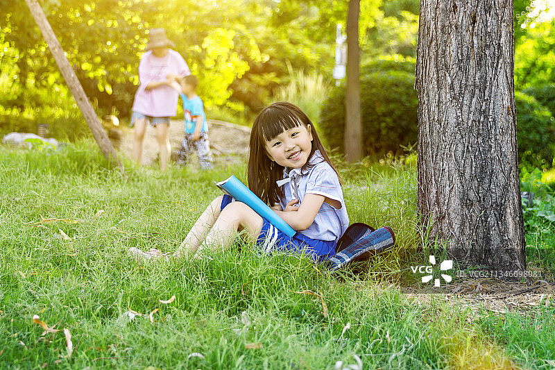 坐在公园草地上大树下看书的小学生图片素材