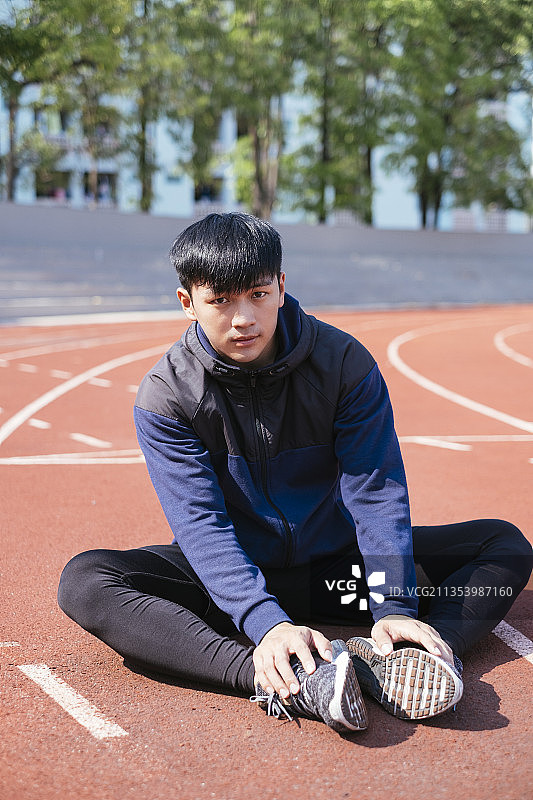 运动亚洲泰国男子在黑色运动服坐在跑道上。图片素材