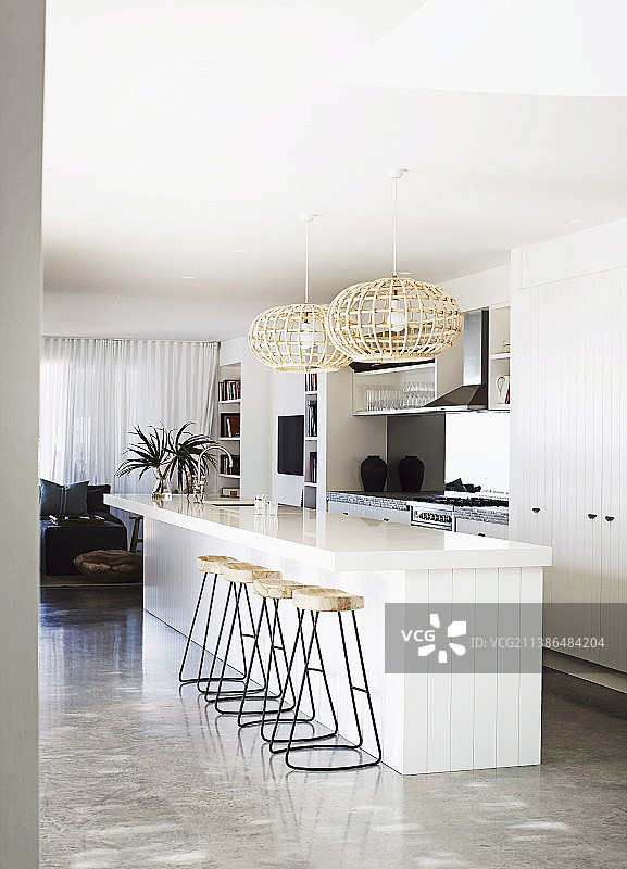 在设计师公寓里，白色的独立厨房柜台上有金属框架的吧台，下面是柳条吊灯图片素材