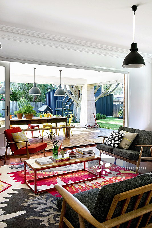舒适的休息室，50年代的沙发和扶手椅，五颜六色的现代地毯和花园一览无余的景色图片素材