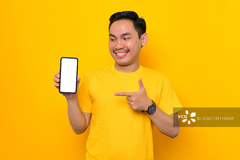 欢快的年轻亚洲男子展示手机与黑屏孤立在黄色背景，印度尼西亚图片素材