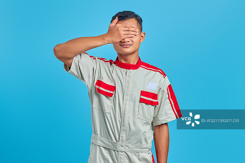 年轻的亚洲机械师的肖像覆盖脸与手掌在蓝色的背景，印度尼西亚图片素材