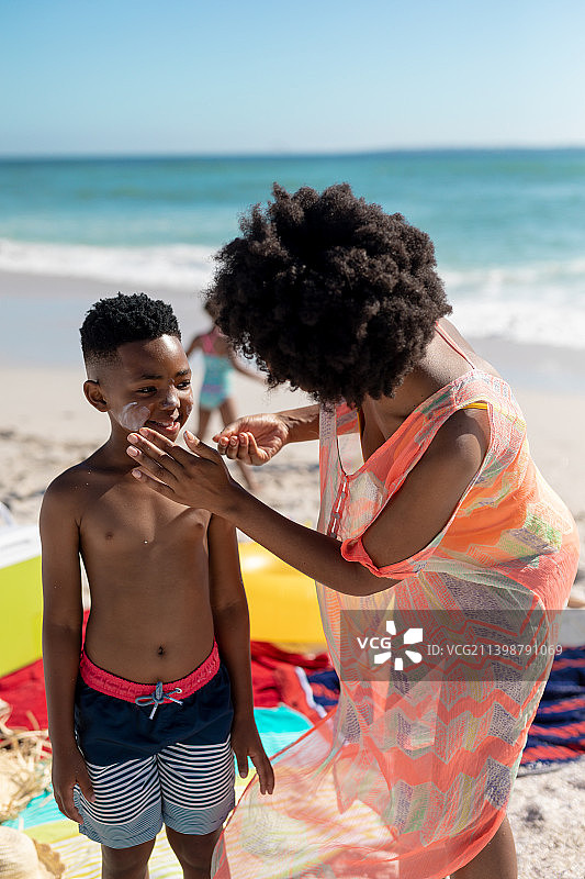 非洲裔美国母亲在海滩上享受暑假的时候给儿子的脸颊涂防晒霜图片素材