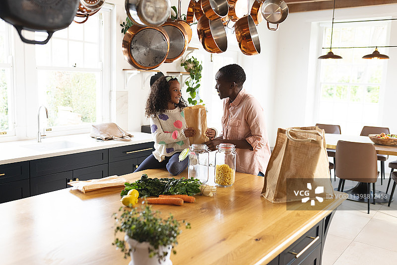 快乐的非洲裔美国母亲和女儿在厨房打开购物袋的图像图片素材
