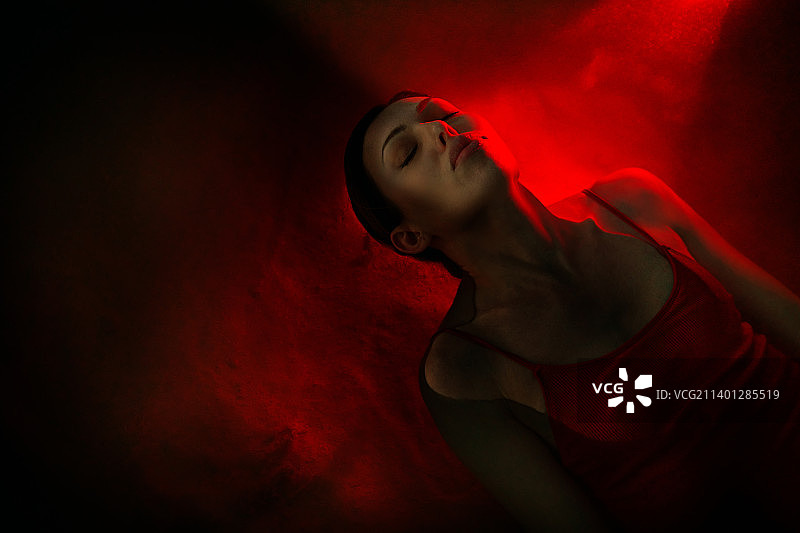漂浮在红色霓虹灯照耀下的水中的女子。宇宙和虚拟现实的概念。图片素材