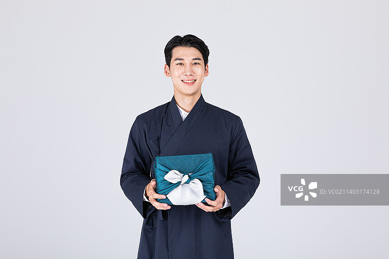 英俊的20多岁的韩国年轻人，穿着现代韩服，穿着韩服，坐着的男人，有传统的盒子和男人的化妆品和鞋子图片素材