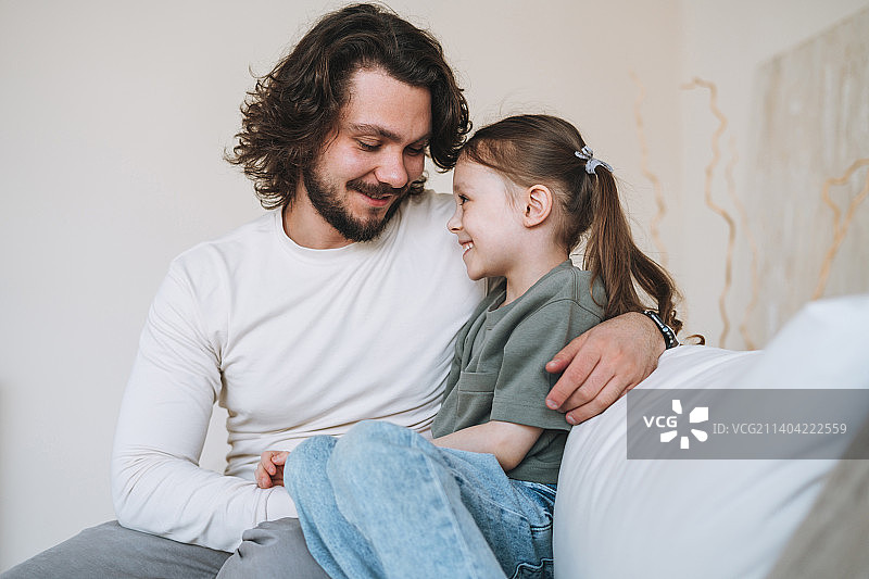 年轻幸福的家庭与父亲和女儿坐在沙发在舒适的家，父亲节图片素材