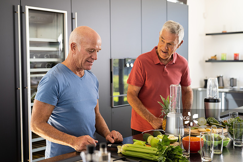 快乐的资深白人男性朋友在厨房里聊天，一起准备健康的冰沙图片素材