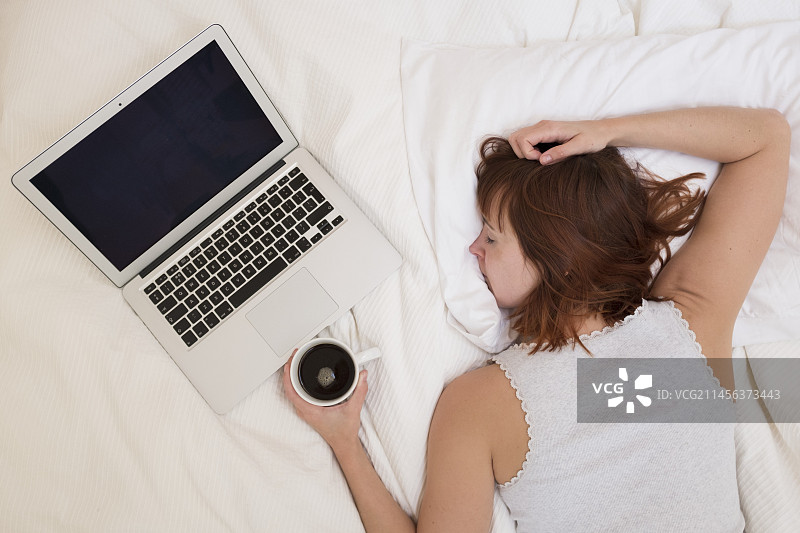 疲惫的女人躺在床上拿着笔记本电脑图片素材