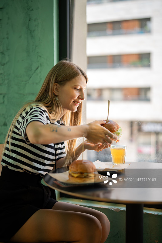 年轻女子在餐厅窗台边吃大汉堡的肖像图片素材