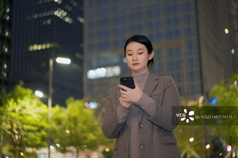 职业女性在夜间在城市街道上使用智能手机图片素材