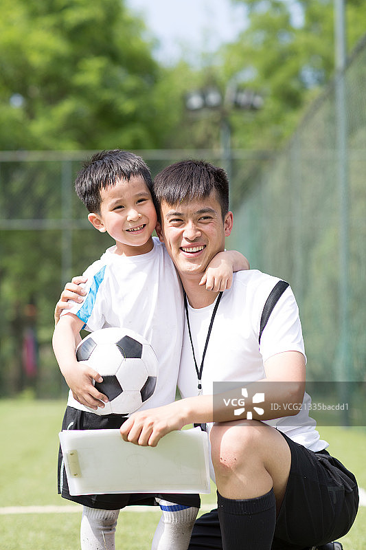 男孩搂着教练在足球场上图片素材