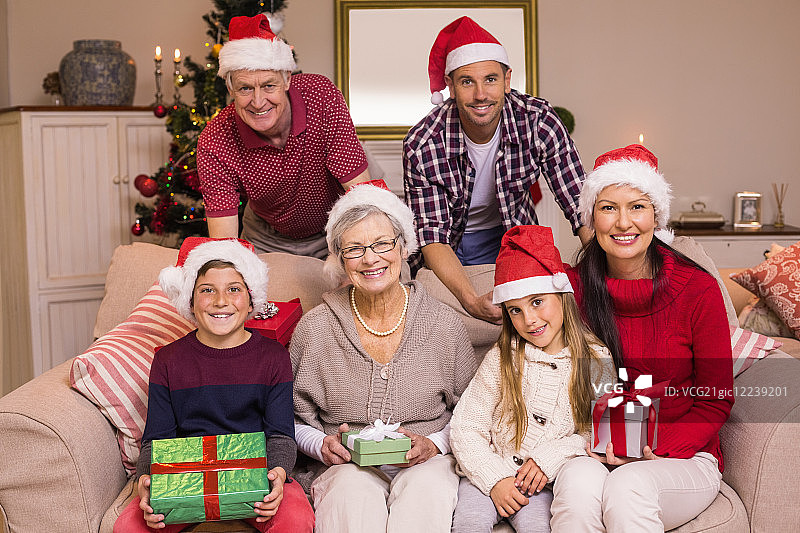 在客厅里，一个快乐的大家庭戴着圣诞帽，拿着礼物图片素材