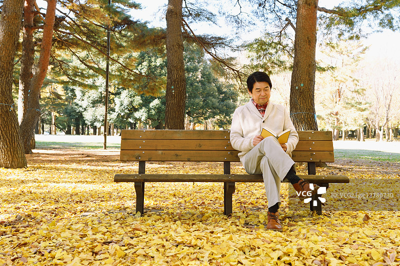 一名日本老人坐在长椅上，手里拿着一本书图片素材