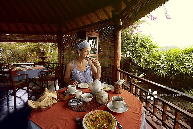 印度尼西亚巴厘岛，一个女人在酒店阳台上吃早餐图片素材