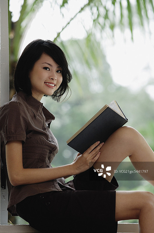 一位女士一边看书一边对着镜头微笑图片素材
