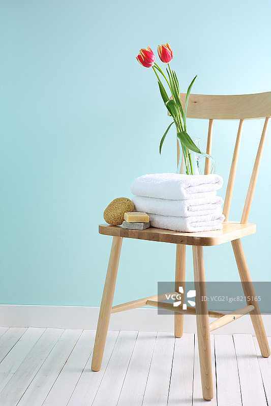 折叠的毛巾、肥皂、丝瓜络和装着郁金香的玻璃瓶放在木椅上图片素材