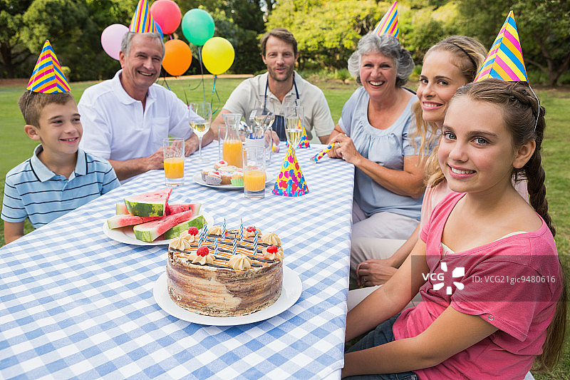 大家庭在野餐桌上庆祝小女孩的生日，对着镜头微笑图片素材