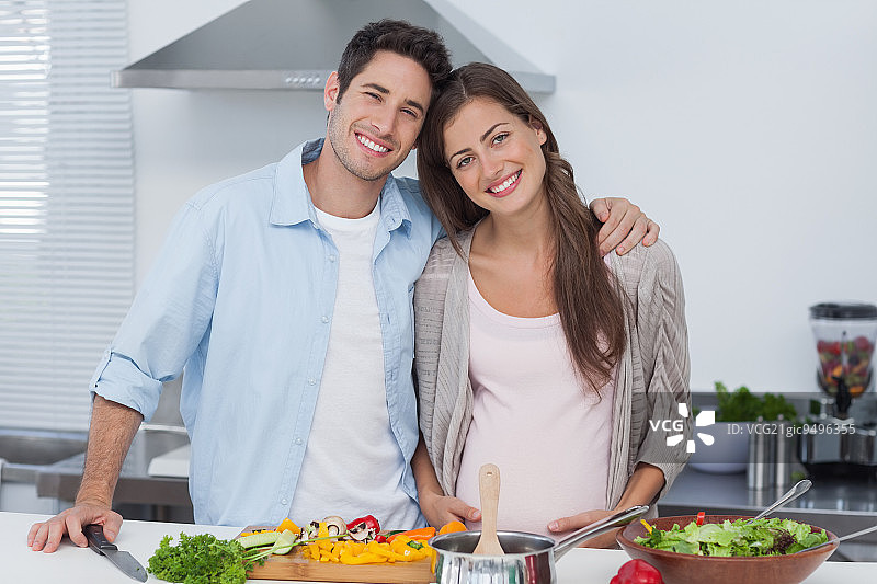 一个男人和他怀孕的伴侣站在厨房里的肖像图片素材
