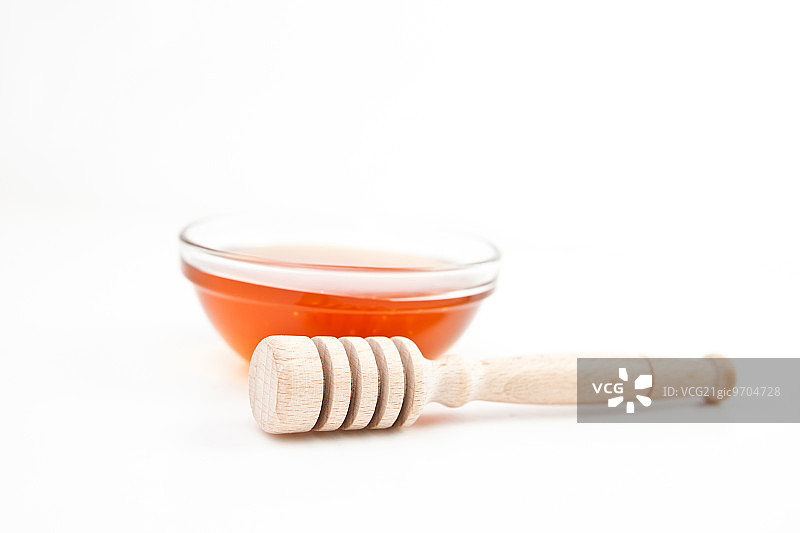 白色背景下，蜂蜜勺后面的蜂蜜碗图片素材