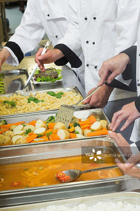 在商业厨房里，厨师们站在供应蔬菜酱汁和意大利面的托盘前图片素材