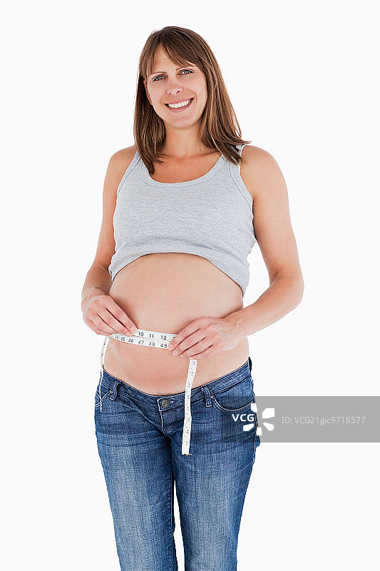 可爱的孕妇站在白色背景下测量她的肚子图片素材